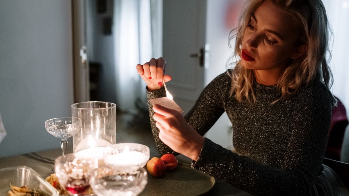 A woman prepares a cozy candlelit dinner table for a special evening indoors.